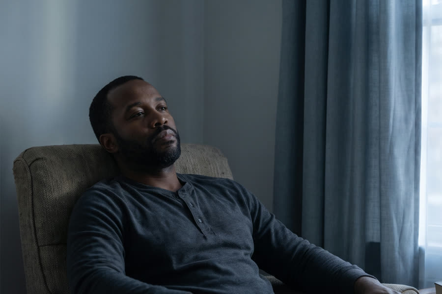 A man sits withdrawn in an armchair in a dim living room