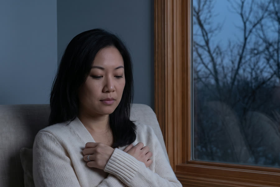 A woman sits guarded by a window in muted evening light